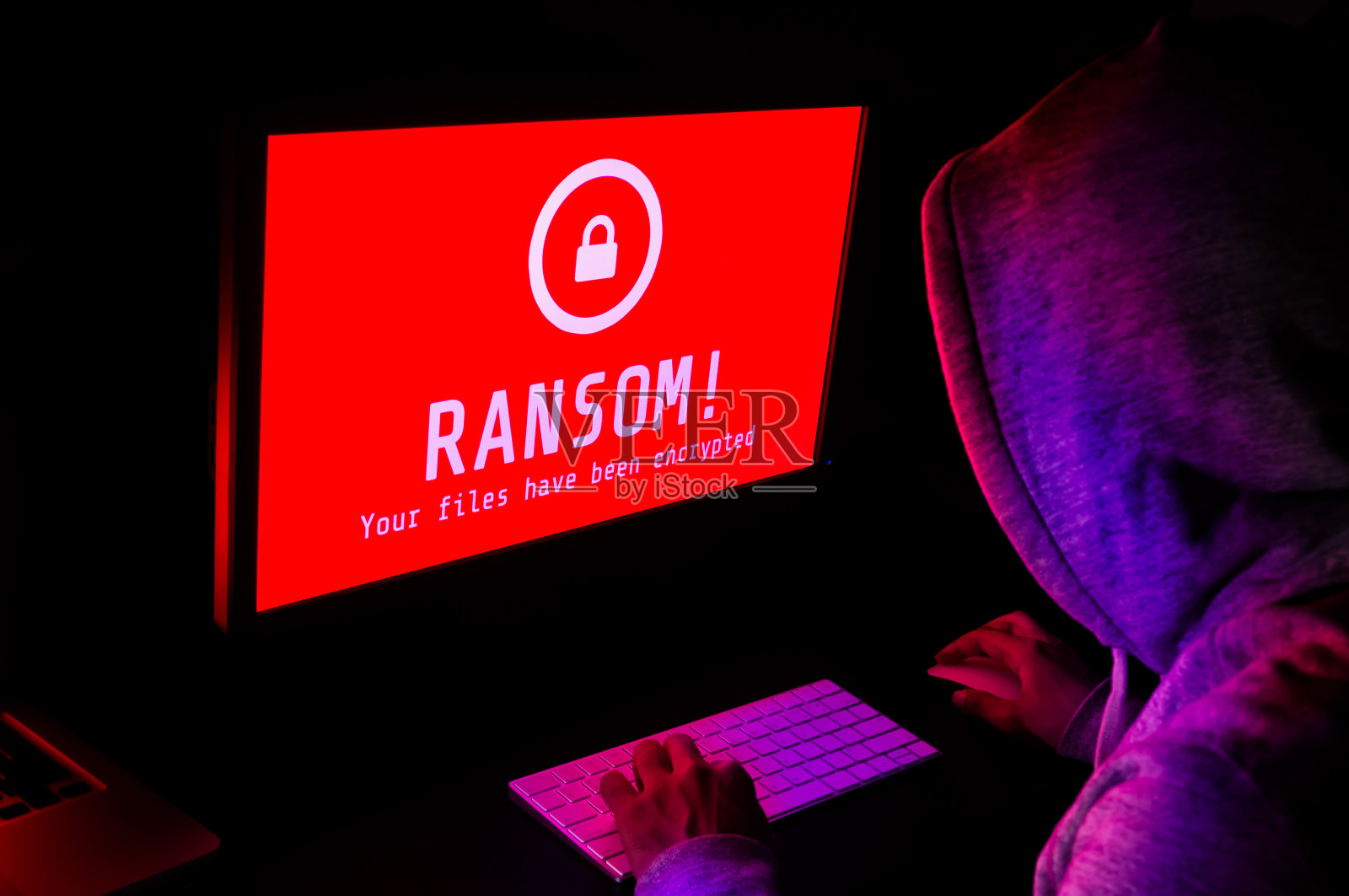电脑屏幕上有红色的勒索软件攻击警报，一名黑客在暗室里敲击键盘，这是在线安全故障和数字犯罪的理想场所照片摄影图片