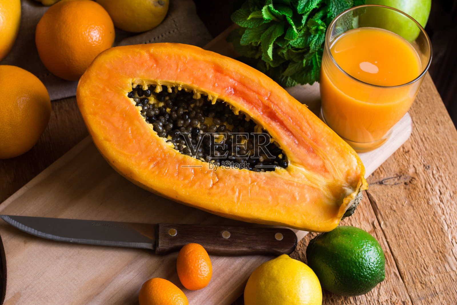 切成两半的熟木瓜，新鲜榨果汁，柑橘类水果，橙子，柠檬，酸橙，金橘，新鲜薄荷放在厨房的桌子上照片摄影图片