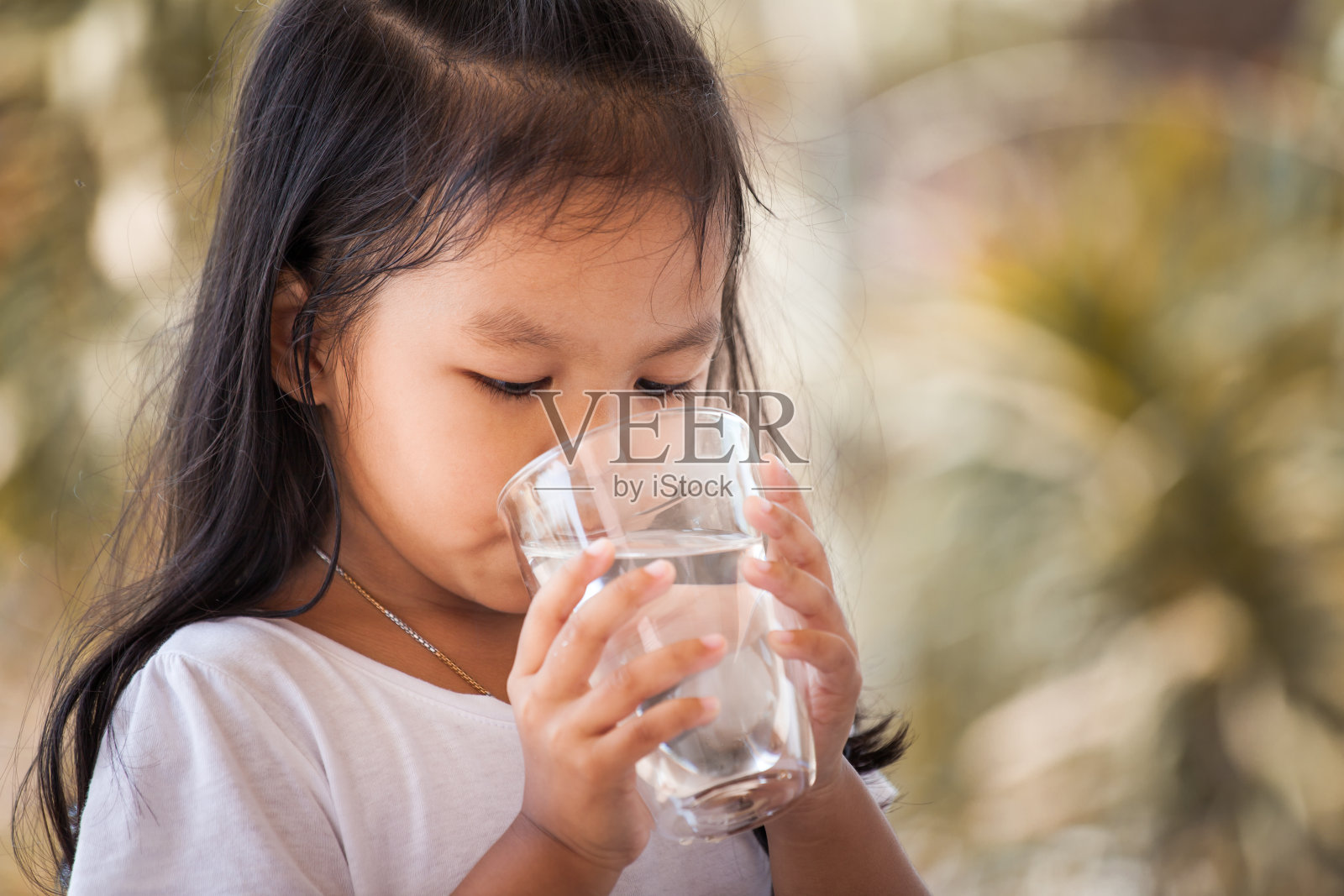 可爱的亚洲小女孩饮用新鲜的水从玻璃在复古色调照片摄影图片