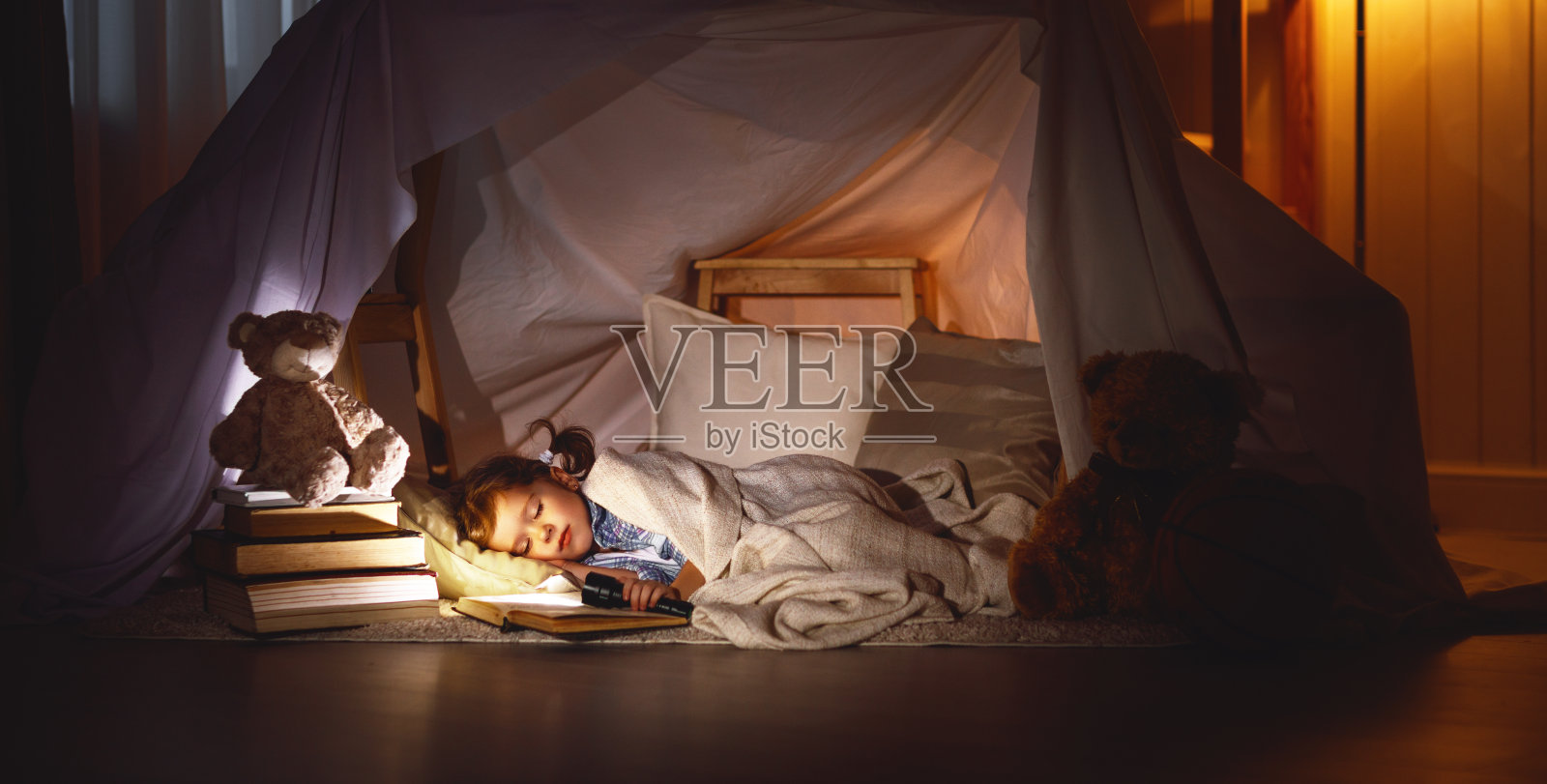 小女孩睡在帐篷里，带着书和手电筒照片摄影图片