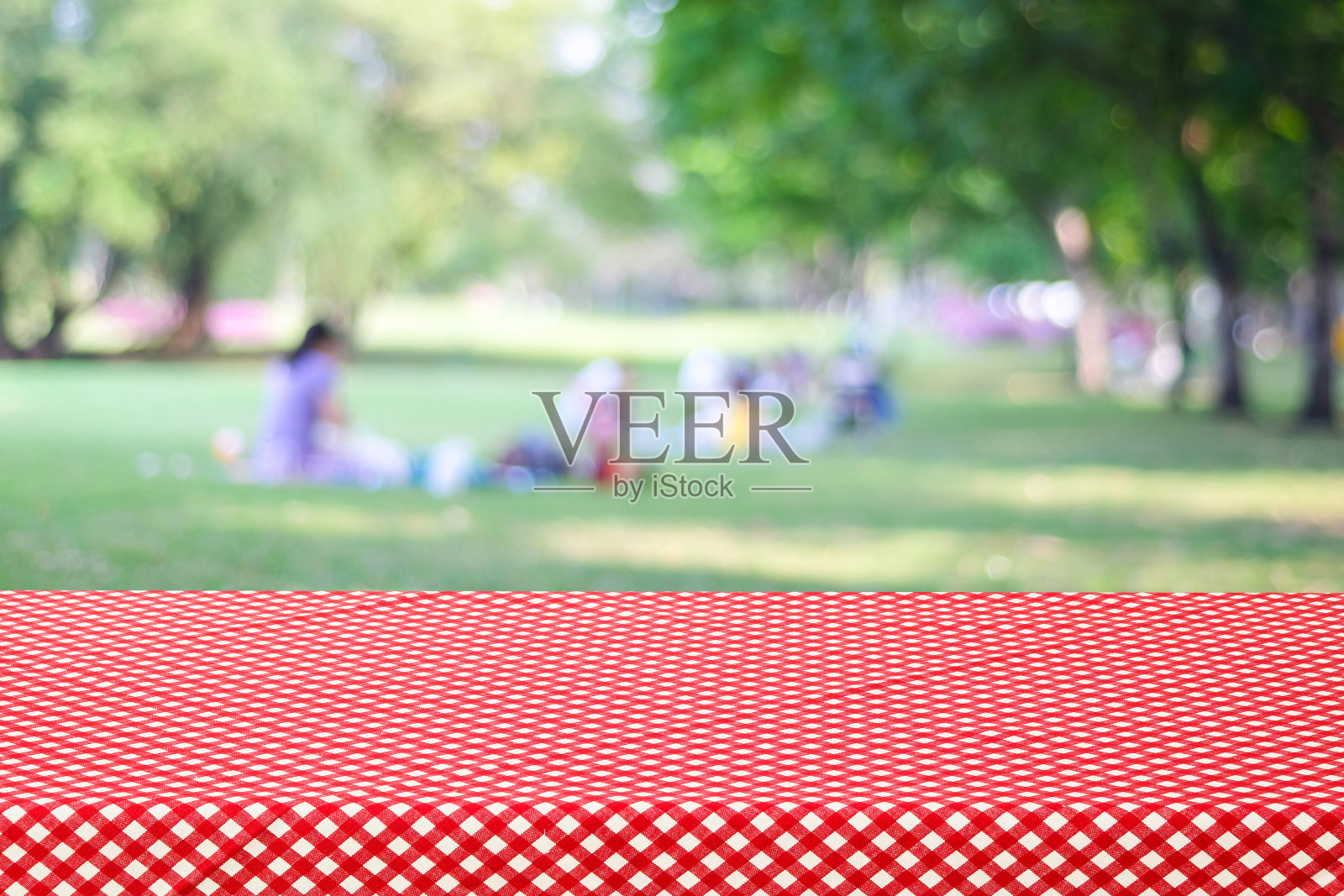 空桌子和红色桌布上模糊公园与人的背景，为产品展示蒙太奇照片摄影图片