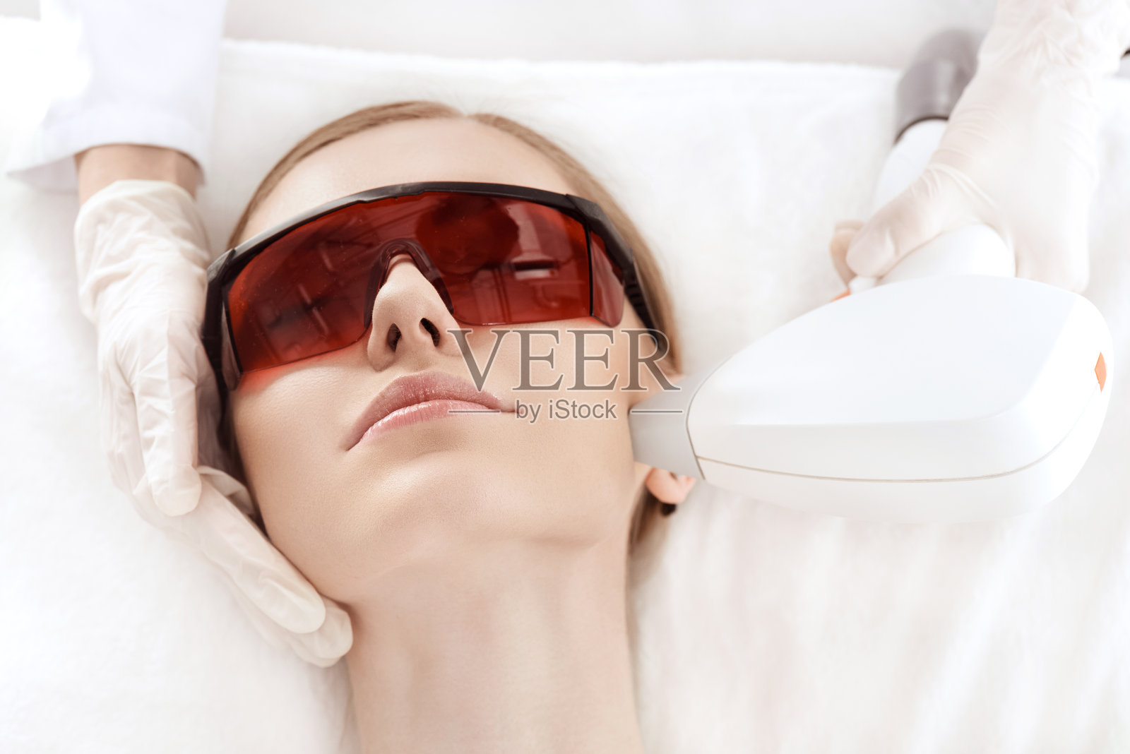 近距离观察年轻女子在紫外线防护眼镜接受激光皮肤护理的脸照片摄影图片