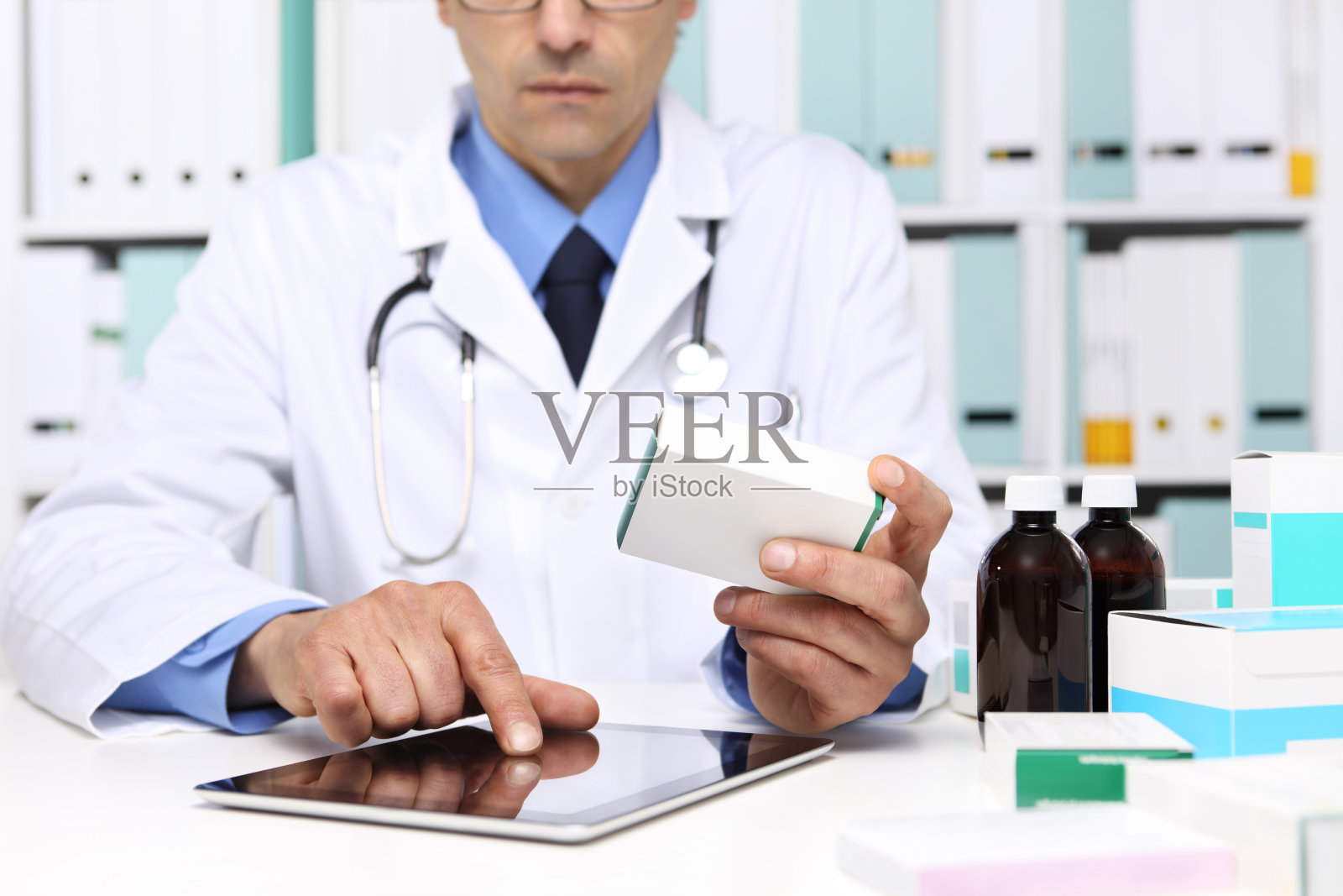 医生阅读数字平板电脑与药盒在办公室的桌面。保健、医疗和制药概念。照片摄影图片