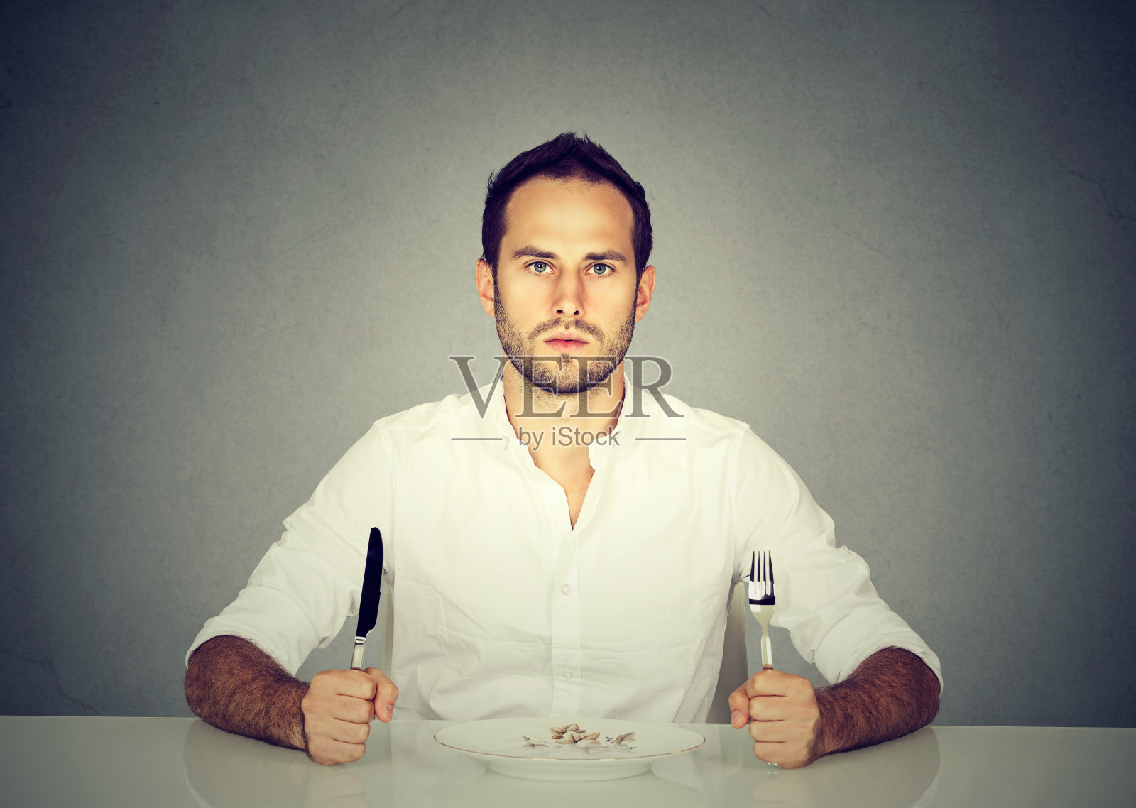 拿着刀叉的男人坐在空盘子的桌子旁照片摄影图片