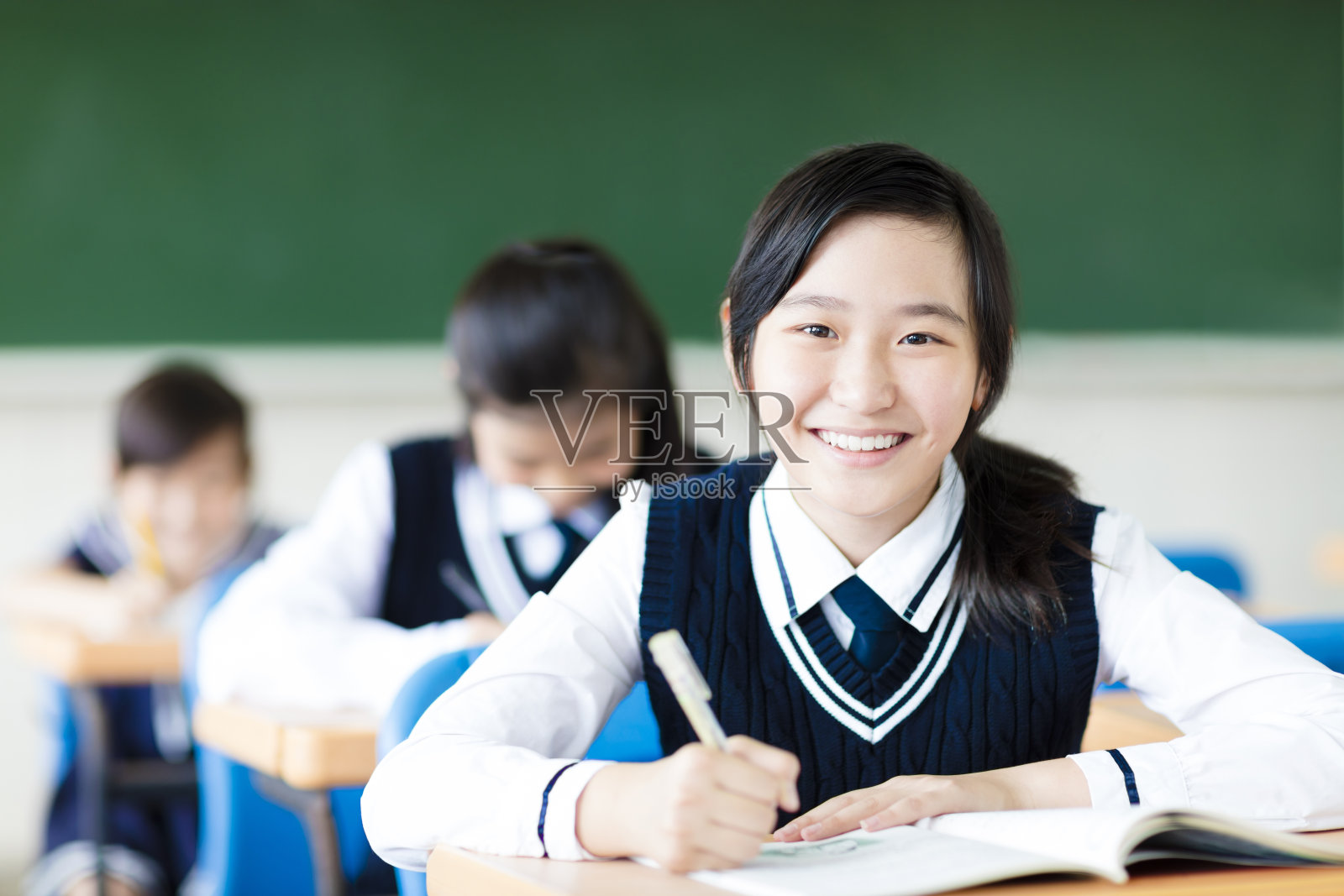 微笑的学生女孩在教室和她的朋友在后面照片摄影图片