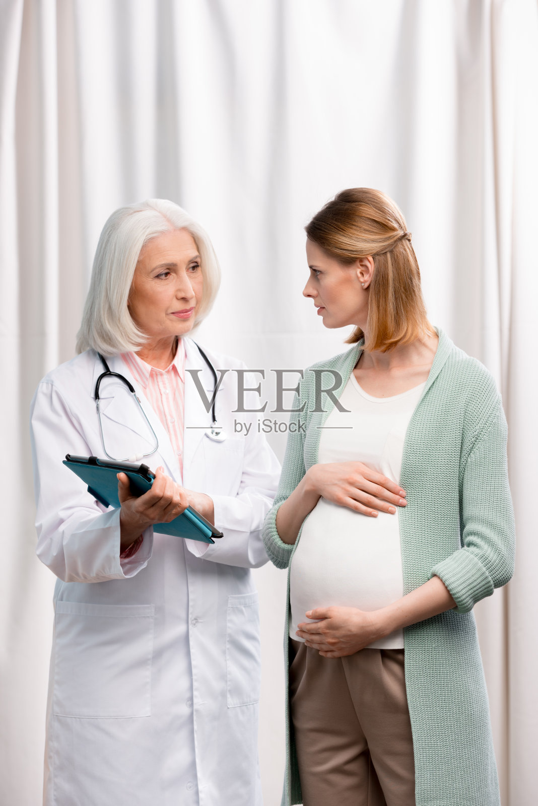 医生拿着平板电脑和年轻孕妇交谈照片摄影图片