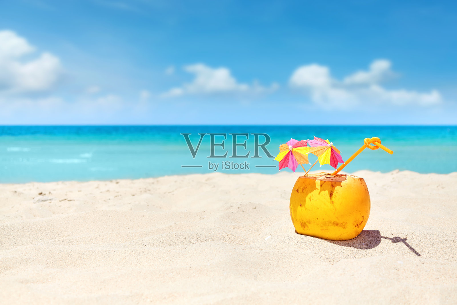 沙滩上的吸管椰子鸡尾酒和五颜六色的雨伞。照片摄影图片