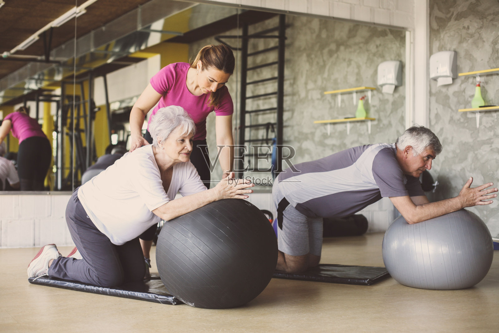 老年人在康复中心锻炼。帮助老年人练习普拉提球的私人教练。照片摄影图片