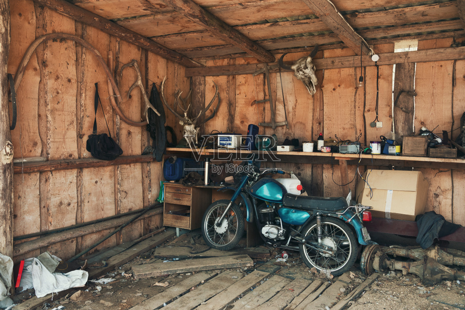 旧蓝-绿色摩托车在风景如画的谷仓。古董摩托车在一个老的机库靠墙鹿角，一个野牛头和许多有趣的稀有物品。仓库在旧谷仓与旧的助力车和木墙。照片摄影图片