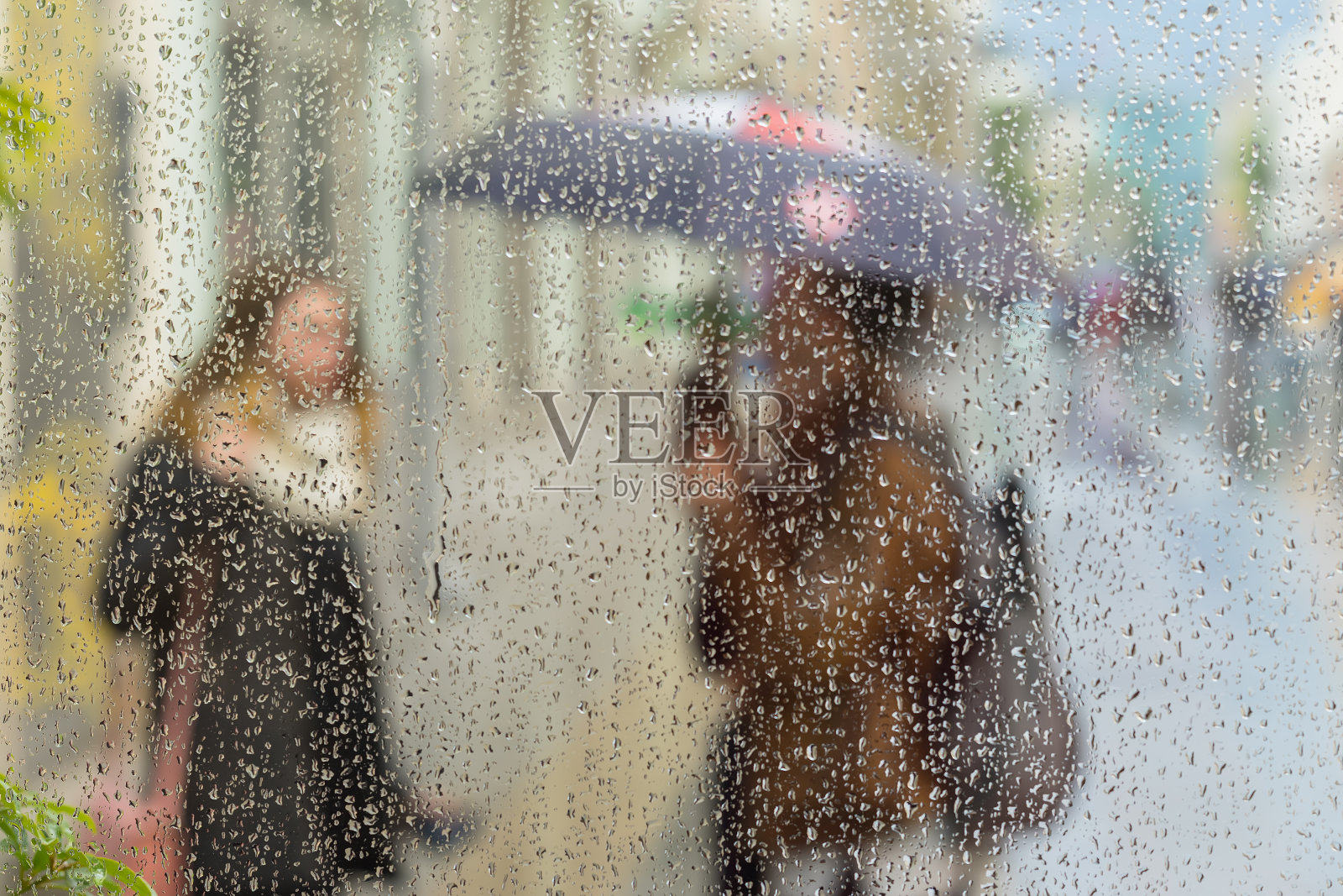 抽象模糊的剪影在雨天的城市里，两个女孩透过窗户玻璃上的雨滴看到模糊的背景、背景、壁纸照片摄影图片