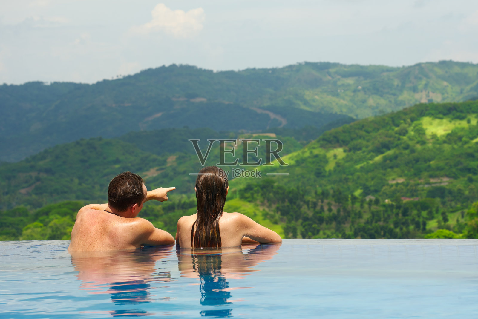 后视图夫妇享受山景观从游泳池照片摄影图片