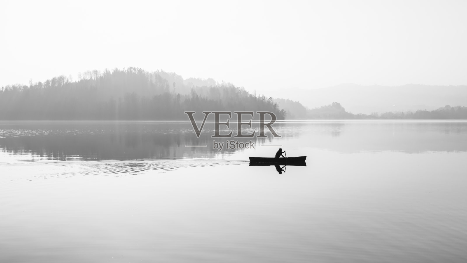 雾笼罩着湖面。一个拿着桨的人在船上。黑色和白色。照片摄影图片
