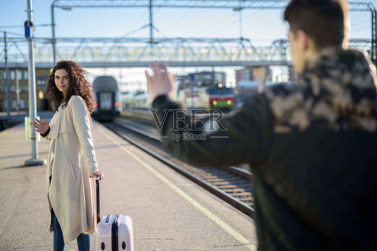 年轻的一对女子带着行李箱在火车站站台离开，男友挥手告别照片摄影图片