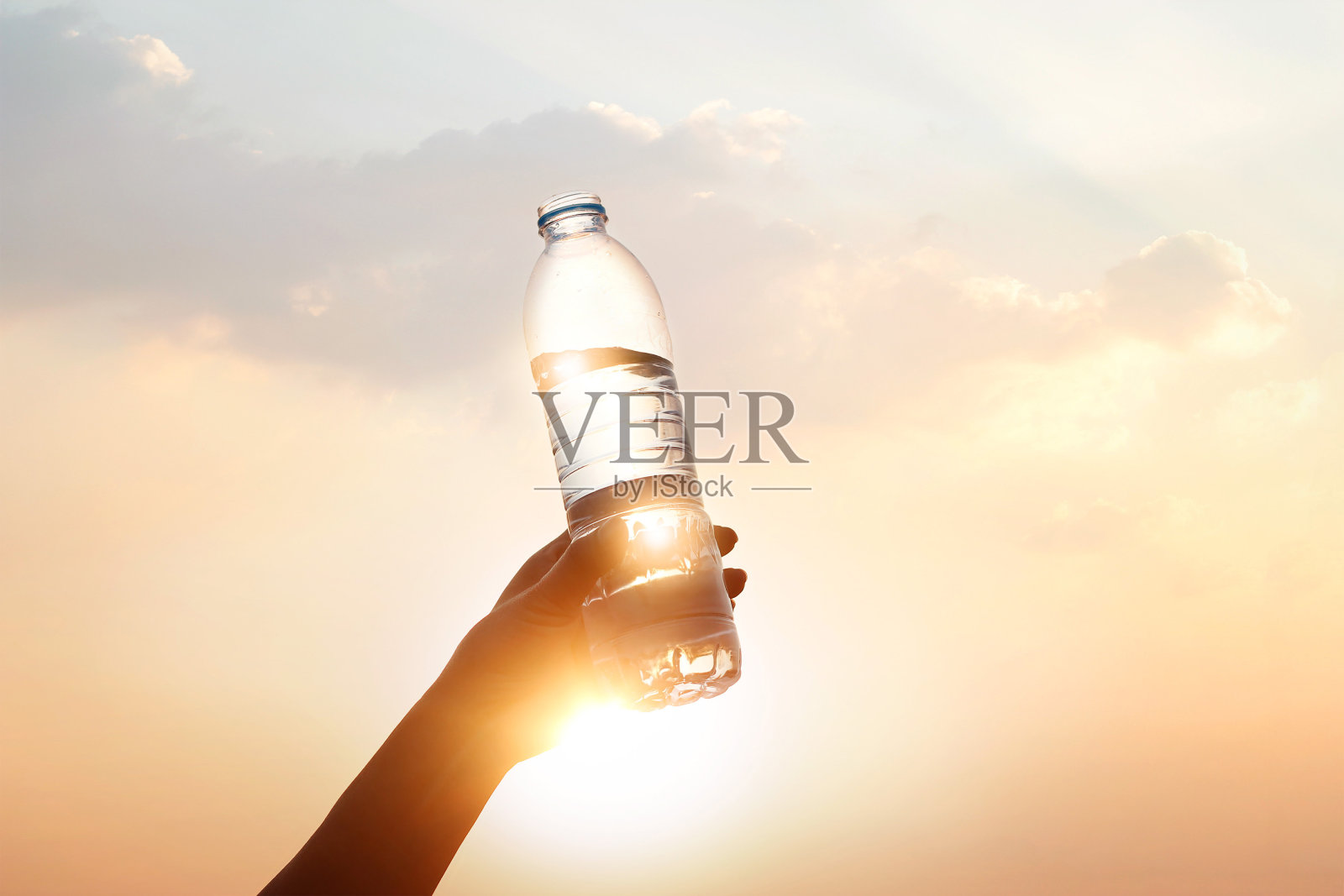 手握饮用水在日落的背景照片摄影图片