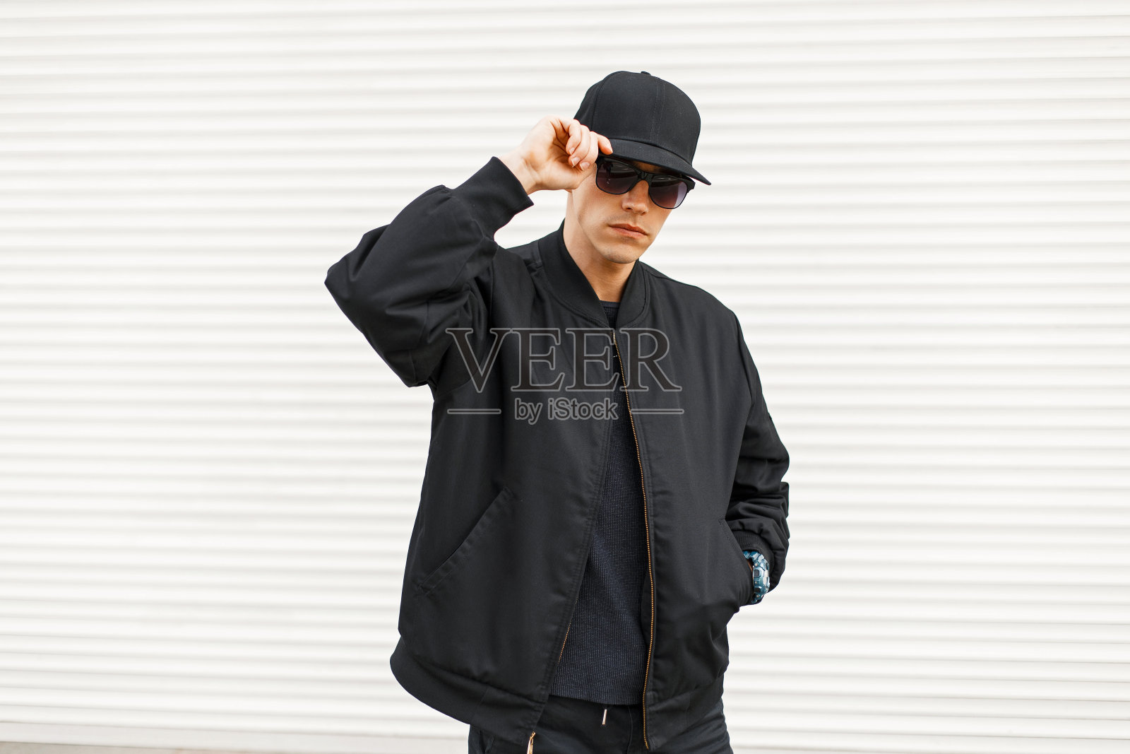 时尚帅气的男人穿着黑色时髦时髦的衣服靠近一堵白色的金属墙照片摄影图片