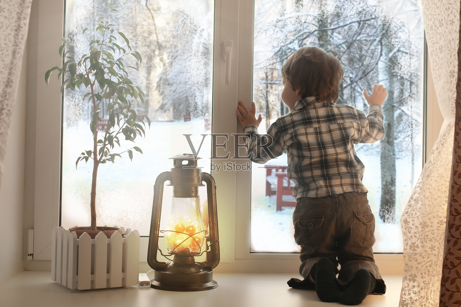 男孩坐在一个白色的窗台上，看着窗外照片摄影图片