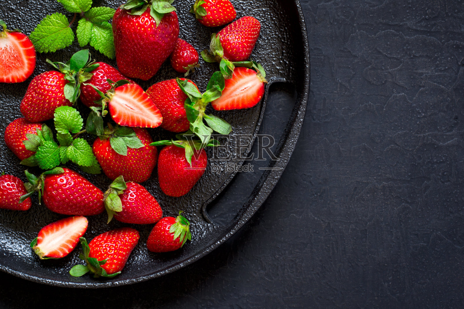 熟透多汁的草莓放在黑色铸铁盘子上。照片摄影图片
