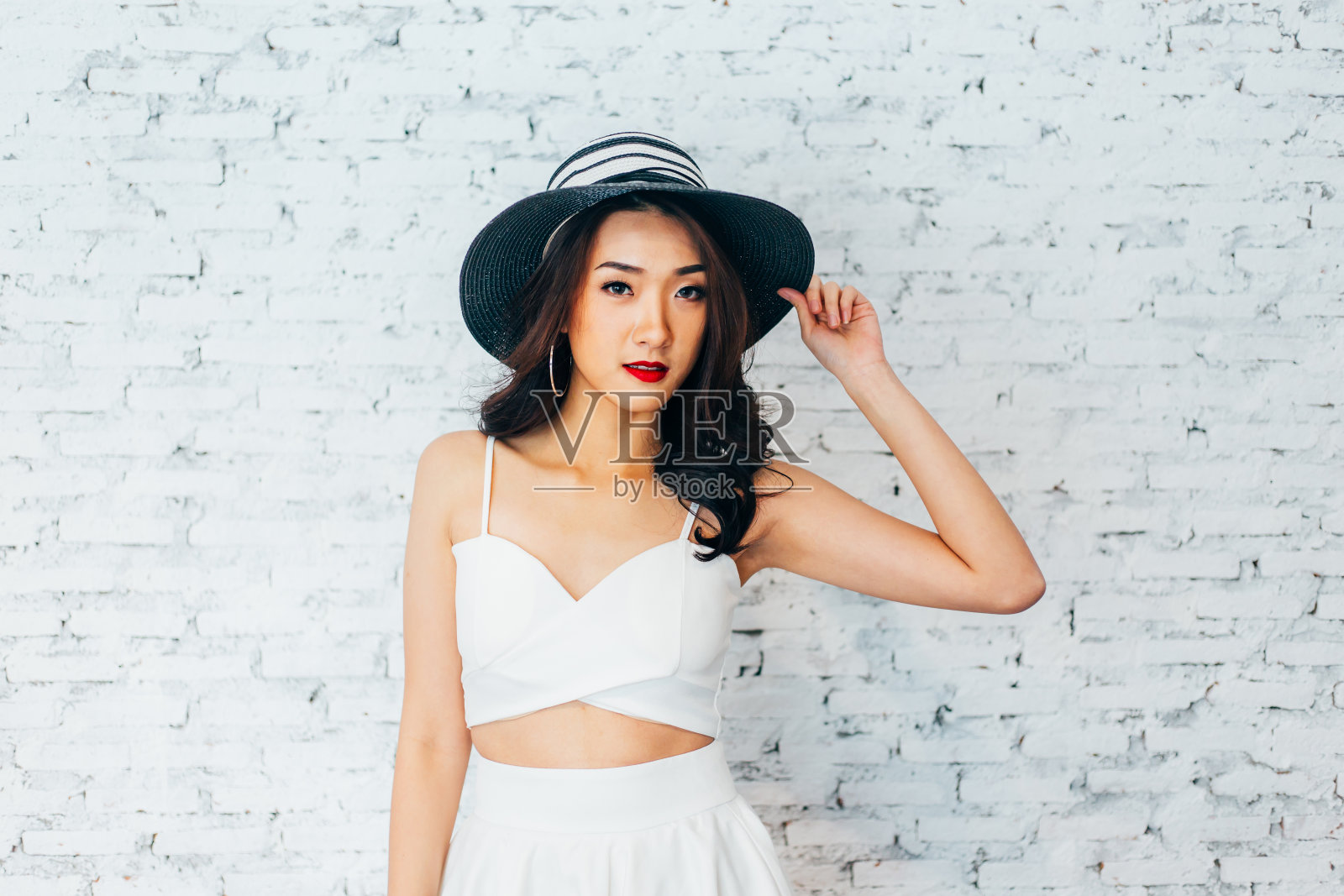 年轻快乐的亚洲妇女微笑在时尚的服装和夏天的帽子在白色砖墙照片摄影图片