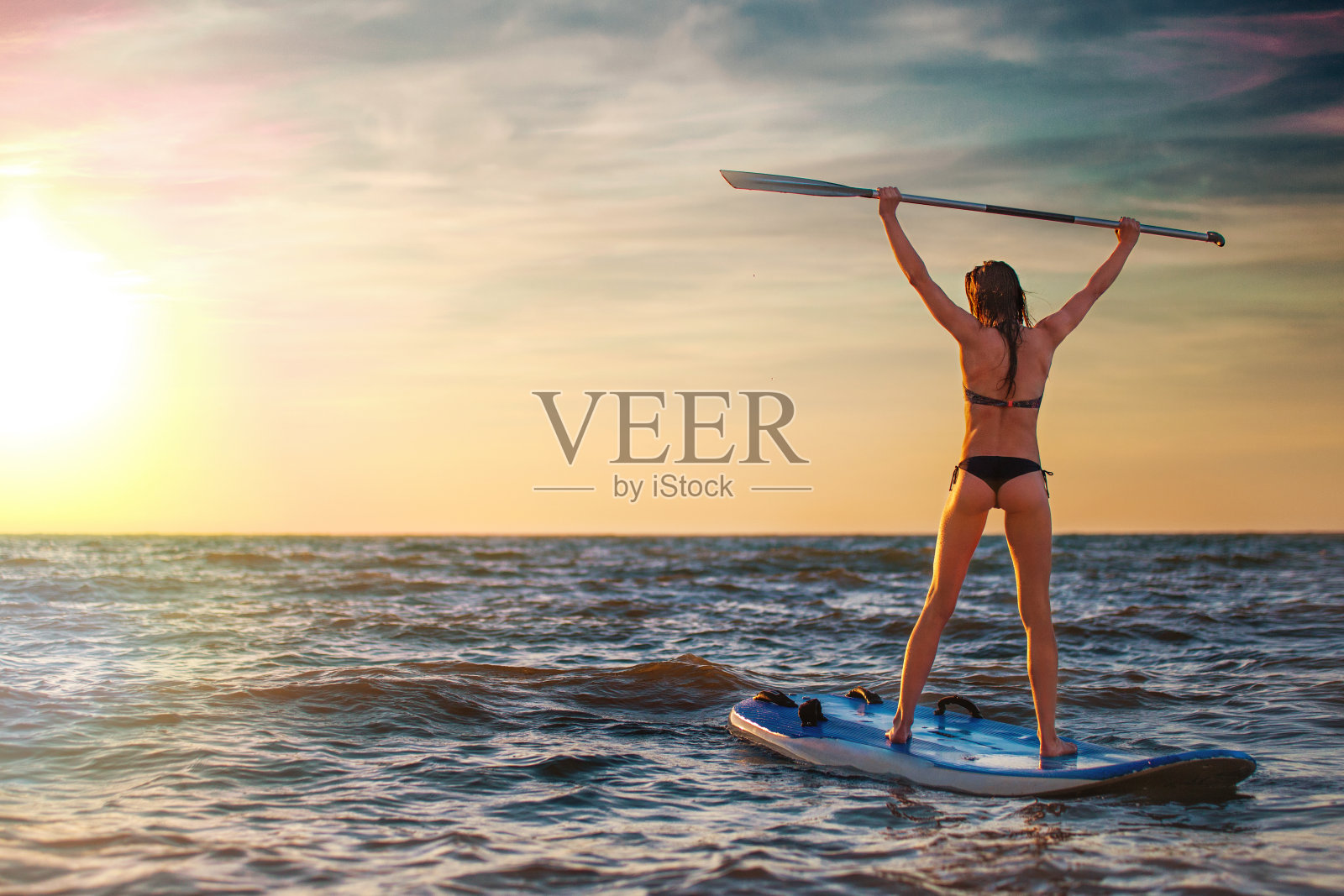 女人练习SUP瑜伽在日落，沉思在一个桨板。照片摄影图片