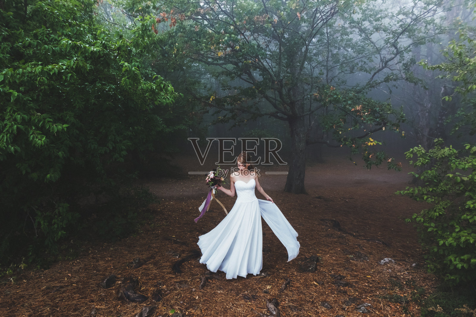 新娘穿着轻盈的衣服在美丽的仙女森林里旋转。雾蒙蒙的秋天的天气照片摄影图片