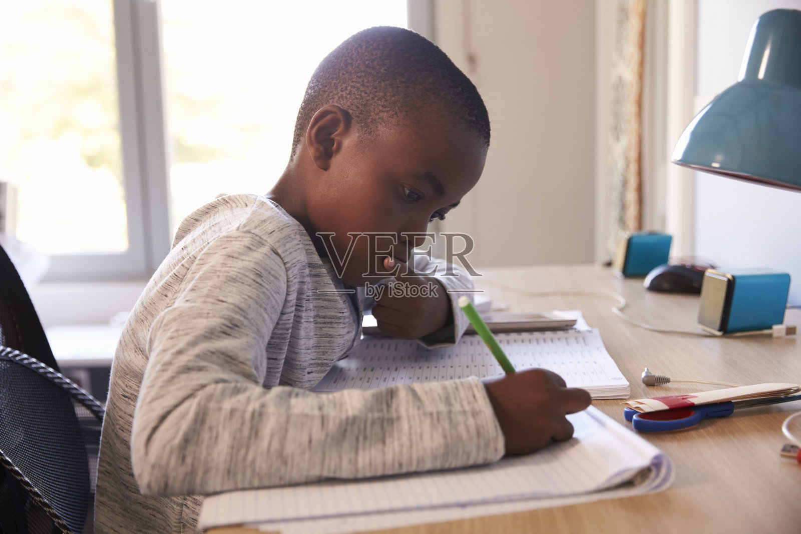 小男孩在卧室里坐在书桌前做作业照片摄影图片