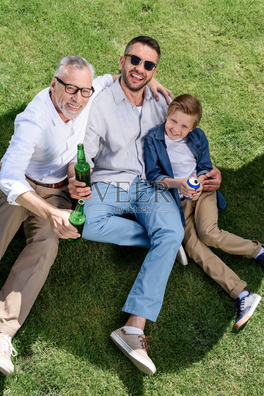 祖父，父亲和儿子喝着啤酒和苏打水，在草地上拥抱照片摄影图片