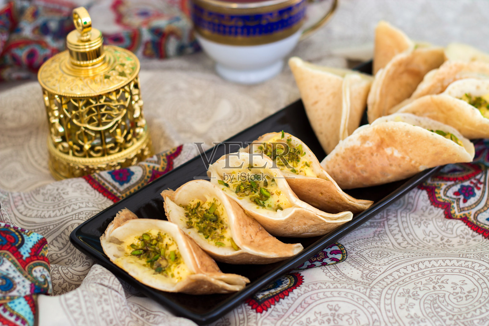 传统的阿拉伯kataif可丽饼塞满了奶油和开心果，斋月开斋时准备的，沉香的金色，在佩斯利的背景照片摄影图片