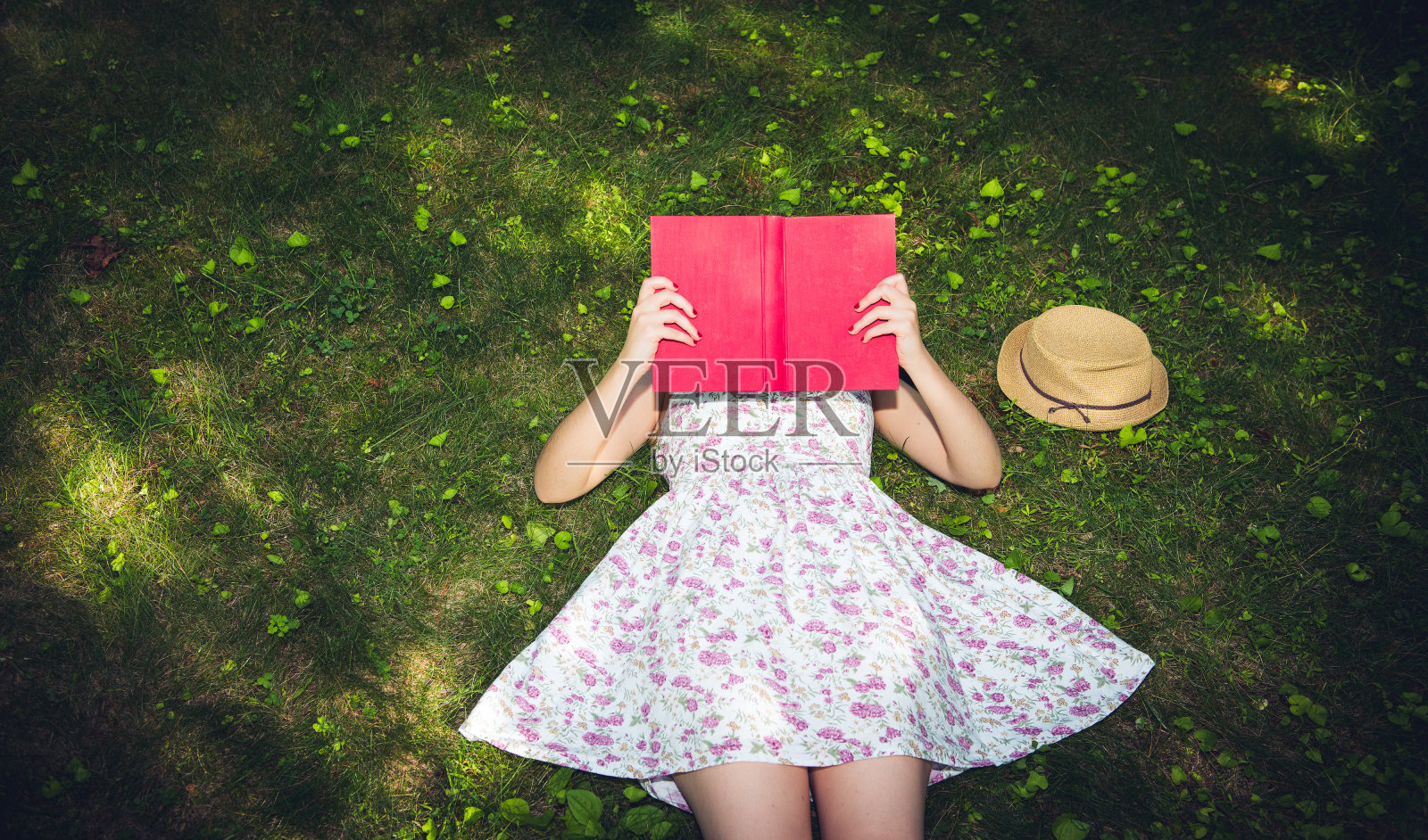 一个女人在外面的草地上看书，捂着脸照片摄影图片
