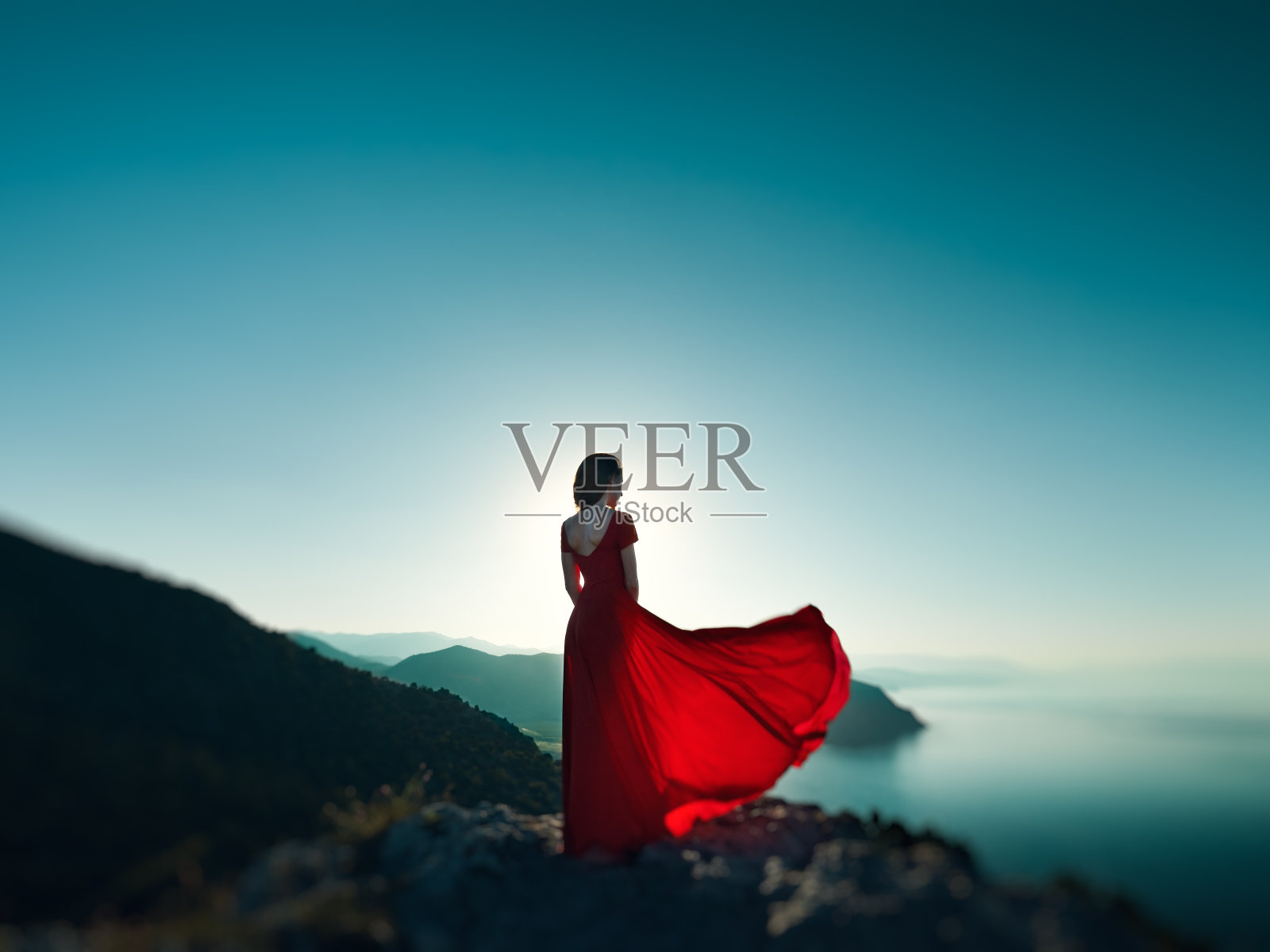 年轻漂亮的女人穿着红色的衣服望着山和海照片摄影图片