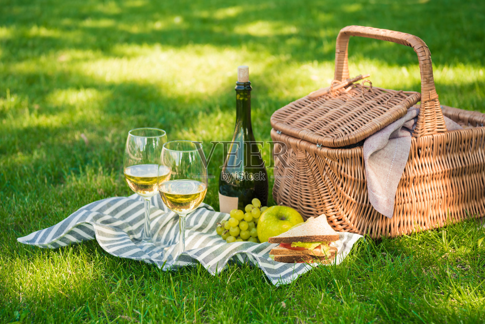 柳条野餐篮子，三明治，水果和酒瓶与餐巾上的杯子照片摄影图片
