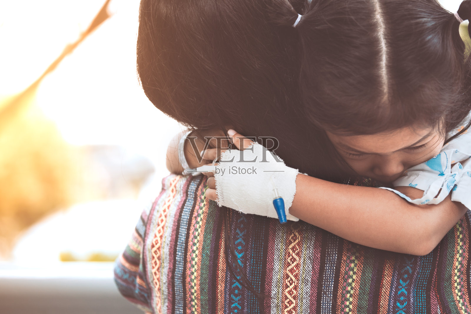 生病的小女孩在医院里拥抱和依靠在她母亲的肩膀上照片摄影图片