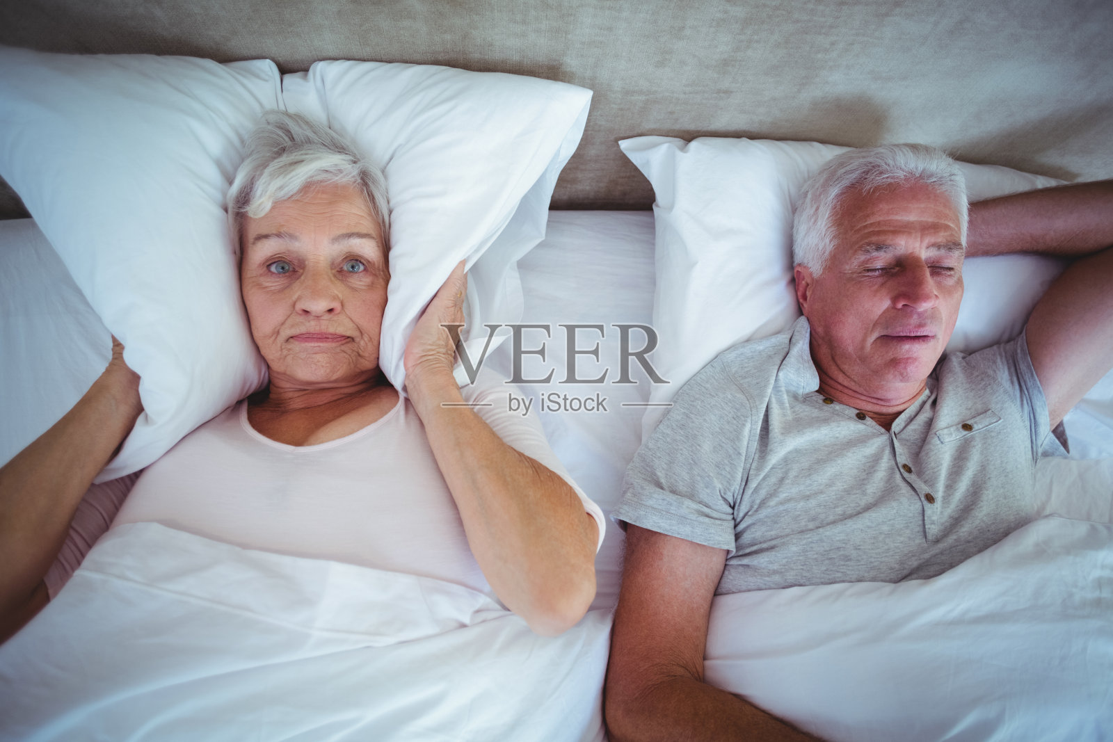 丈夫在床上打鼾，妻子用枕头堵住耳朵照片摄影图片