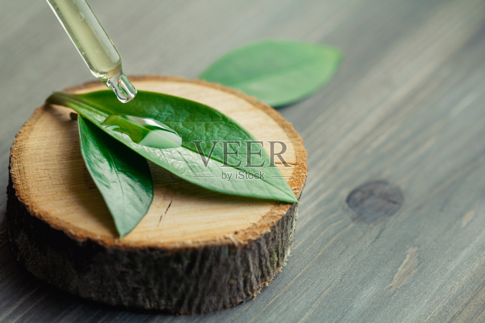 特写化妆油从吸管滴在绿叶上的一个木制的切割。照片摄影图片