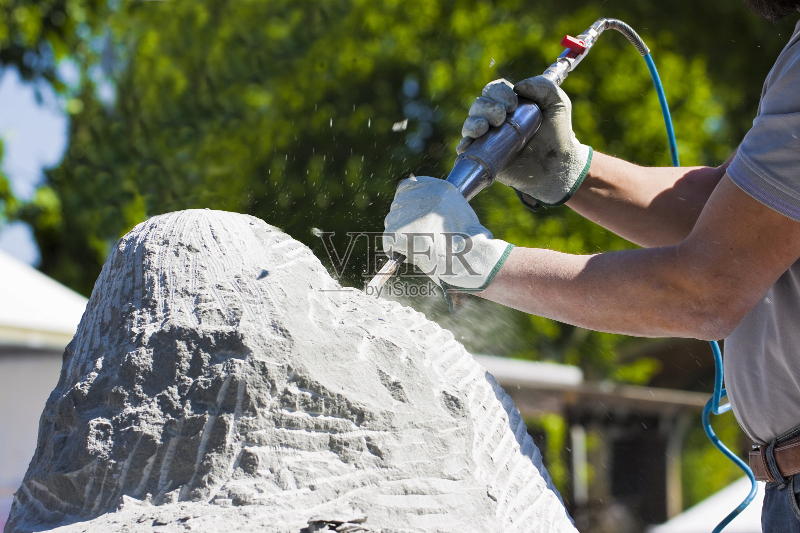 年轻人在工作时用压缩空气的凿子和防护手套雕刻一块石头照片摄影图片