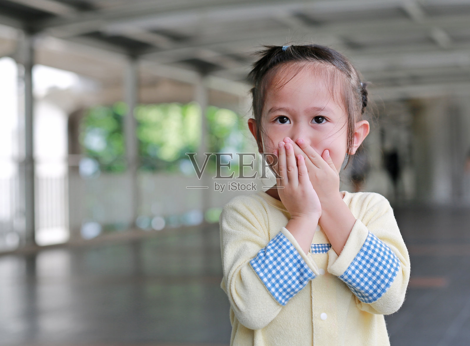 一个亚洲小女孩用手捂住自己的嘴和鼻子。照片摄影图片