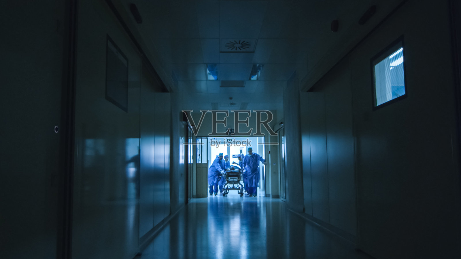 医院急救小组抬着病人担架穿过黑暗的医院大厅。照片摄影图片