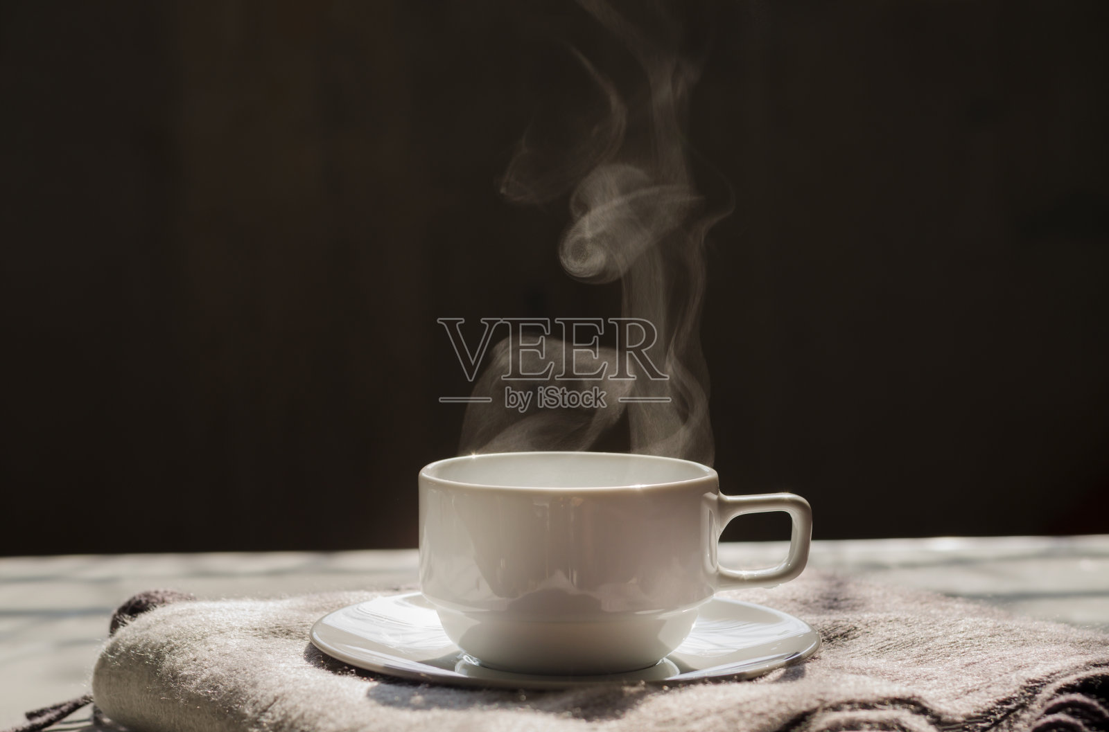 热黑咖啡在白色陶瓷杯和托盘上舒适的羊毛围巾与漂亮的蒸汽温暖的阳光在早上和复制空间的文字，标志或措词插入在深灰色的背景，热饮照片摄影图片