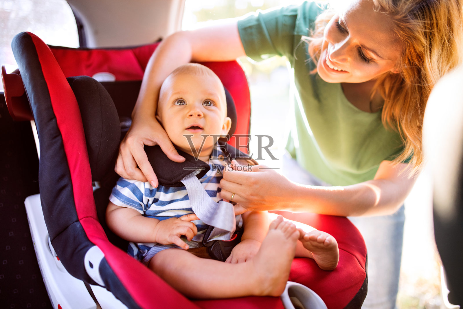 年轻的母亲把小男孩放在汽车座椅上。照片摄影图片