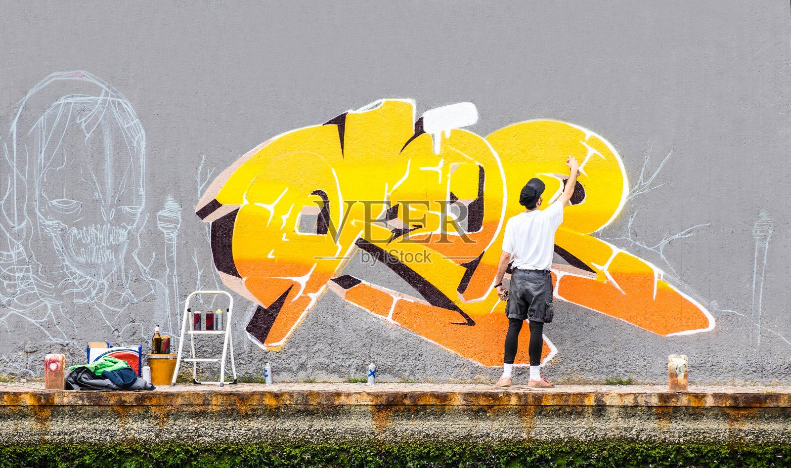 街头艺术家在公共空间墙上画彩色涂鸦-都市男子表演和准备用黄色气溶胶彩色喷雾的活壁画的现代艺术概念-多云的下午滤镜照片摄影图片