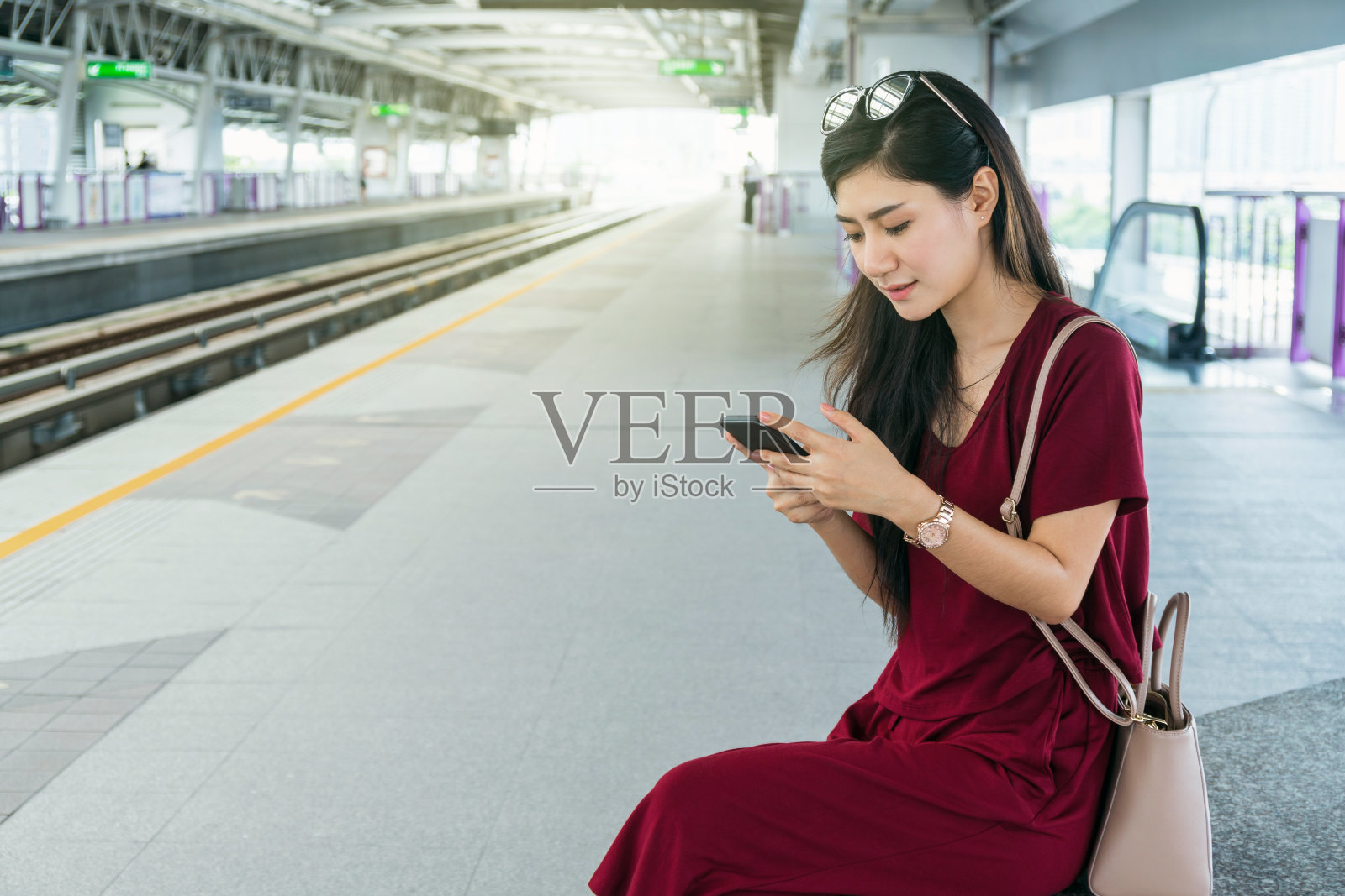 亚洲女性乘客休闲套装通过智能手机在Skytrain轨道或地铁上使用社交网络，在大城市旅行，生活方式和交通理念照片摄影图片