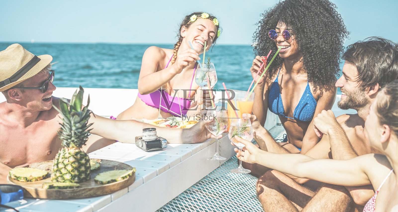 快乐的朋友在船上聚会喝热带鸡尾酒和吃菠萝-年轻人在海上独家旅行的乐趣-青春，友谊和夏季概念-主要集中在非洲女人的脸照片摄影图片