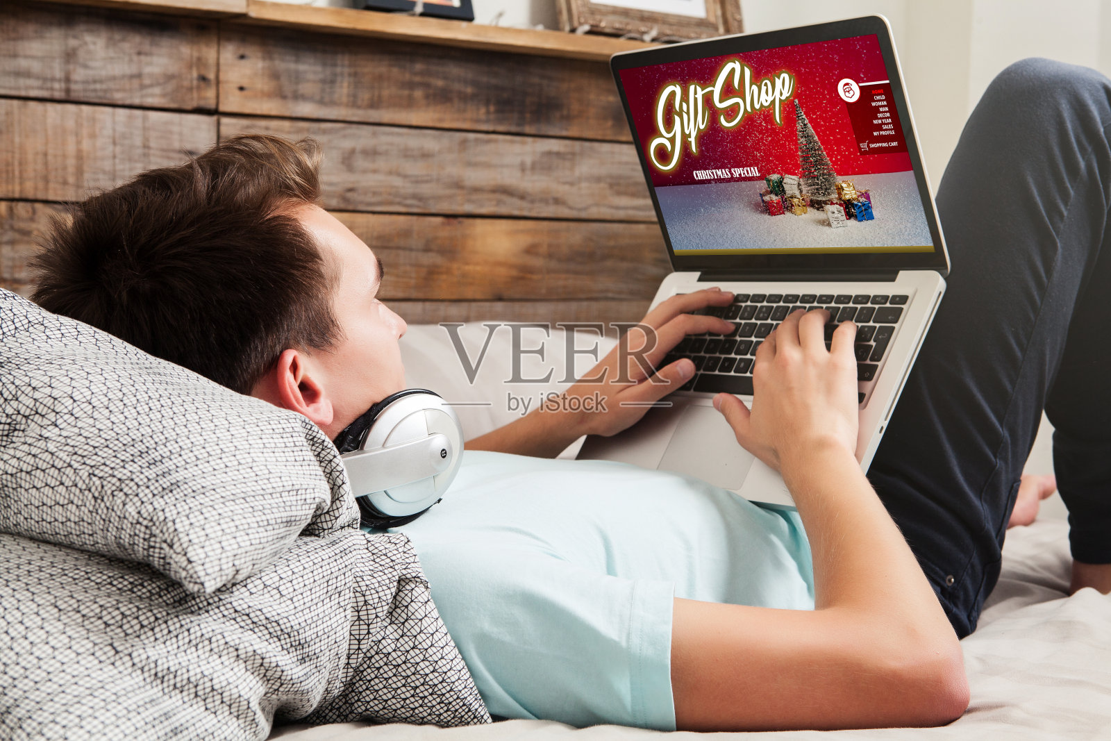 一名男子坐在家里的床上，一边上网一边用笔记本电脑购买圣诞礼物。照片摄影图片