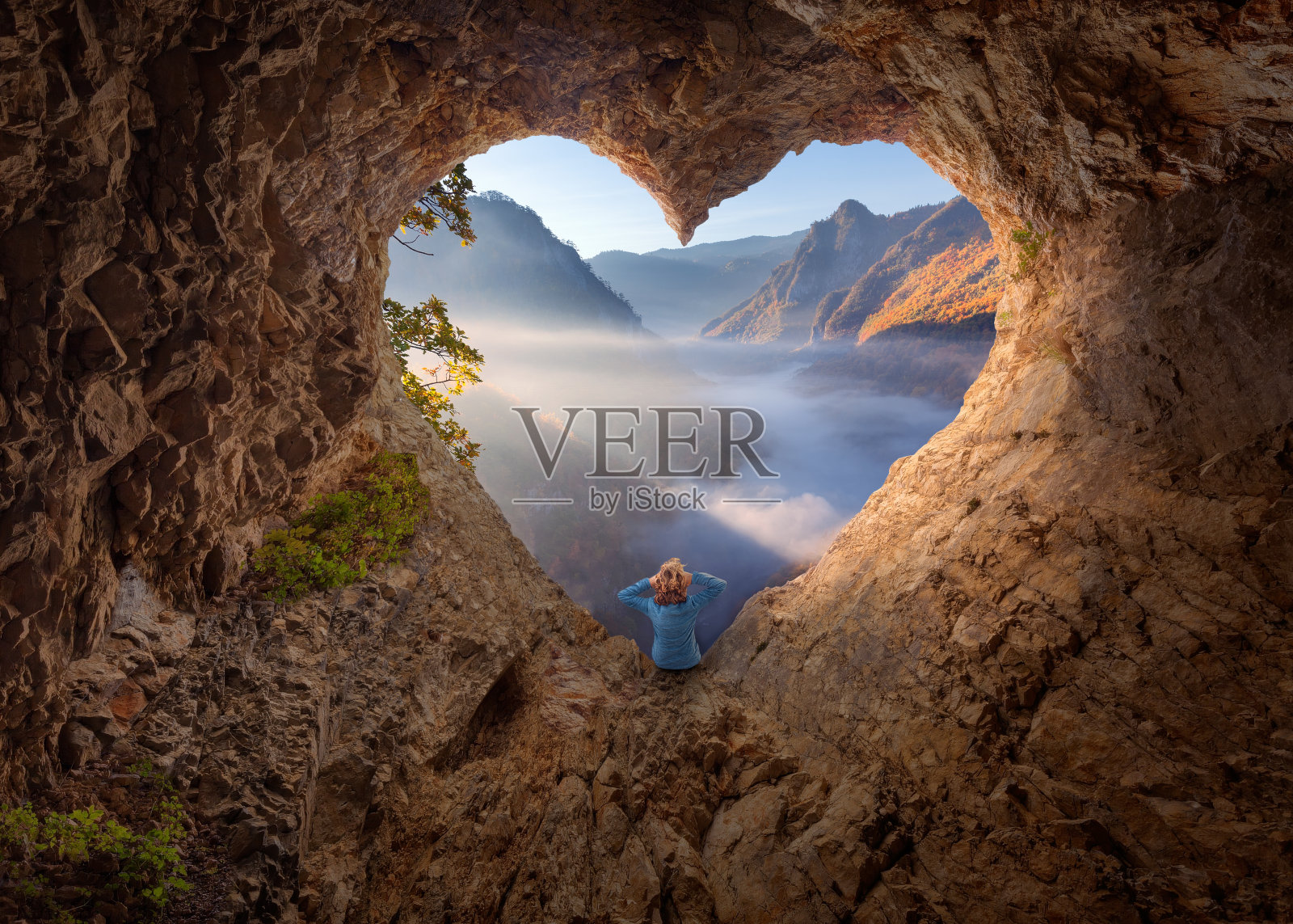 女人在心形的洞穴在清晨看着迷雾峡谷照片摄影图片