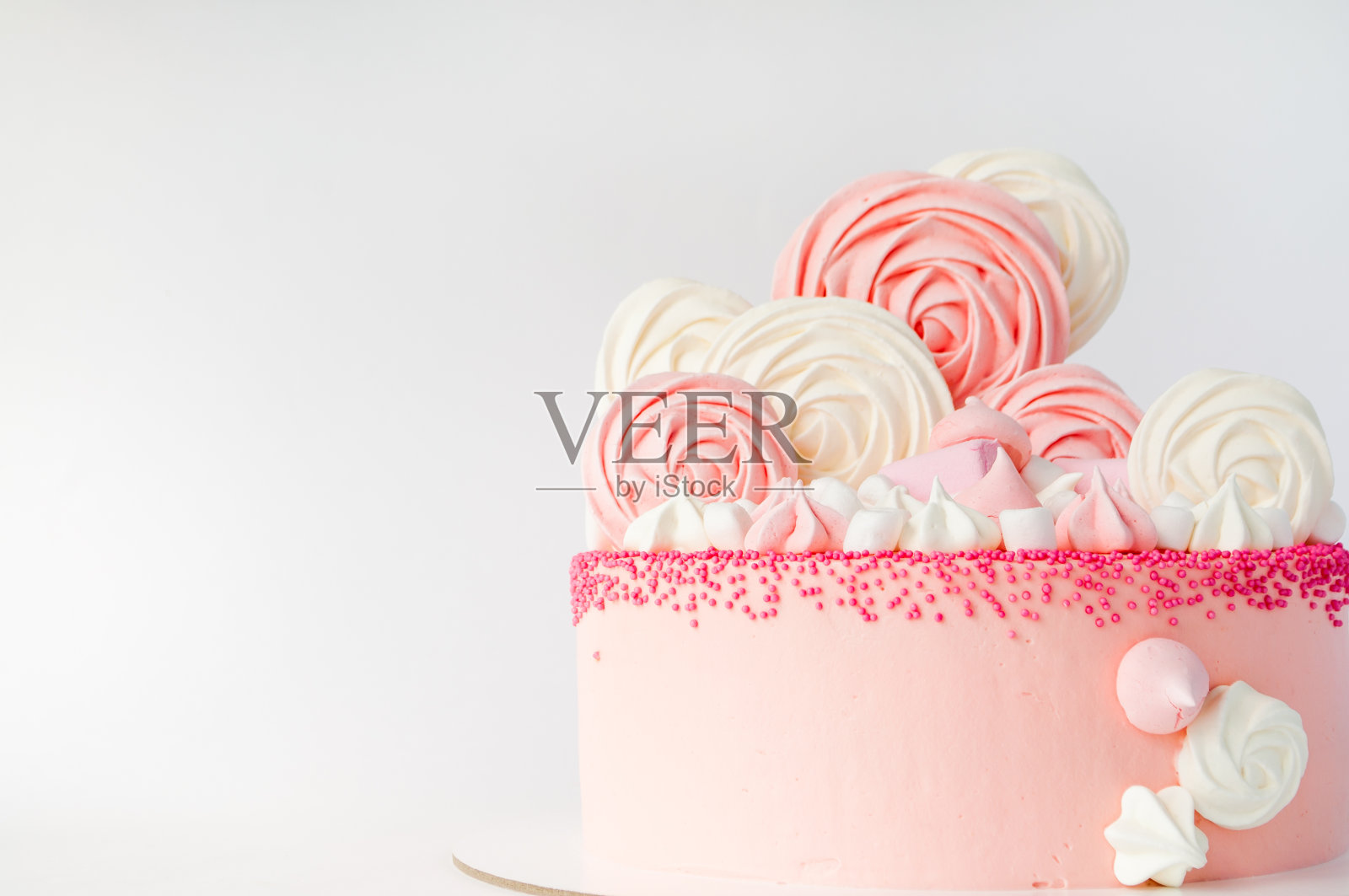 为女孩准备的粉色生日蛋糕，用棉花糖、蛋白酥饼装饰在白色的背景上。照片摄影图片