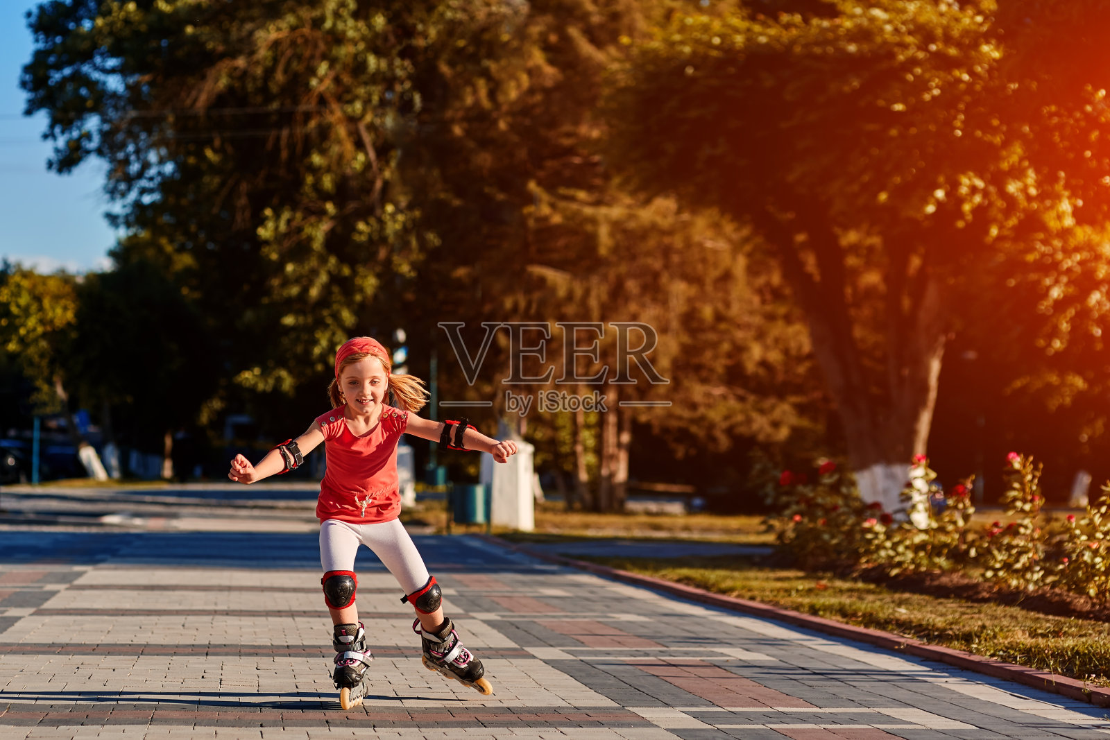 美丽的夏天，在城市公园里，穿着红布的漂亮小女孩在户外学习滑旱冰。照片摄影图片