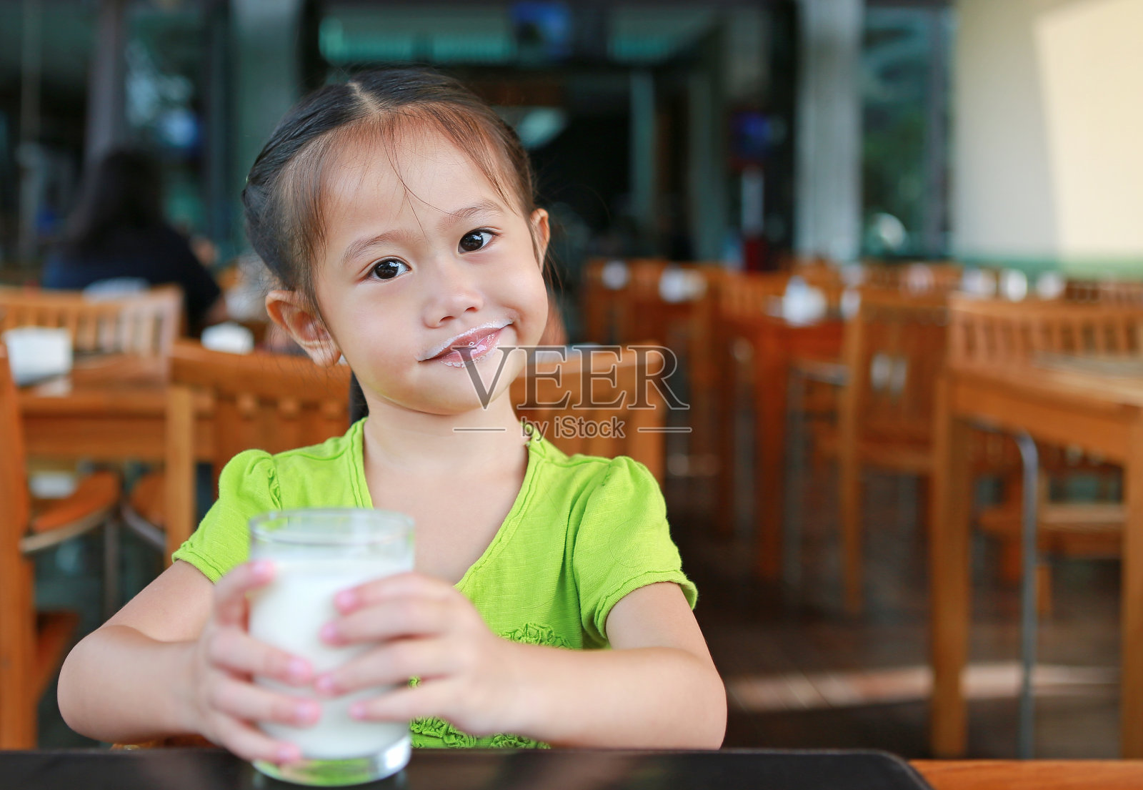 可爱的亚洲小女孩拿着一杯牛奶在咖啡店。照片摄影图片