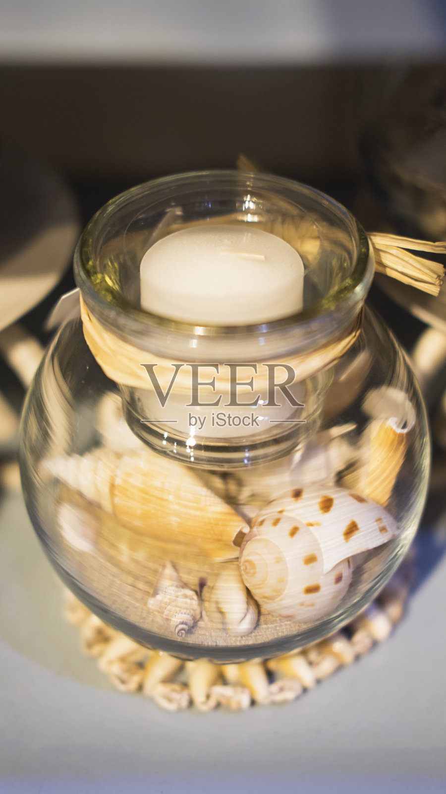 白色的蜡烛放在一个透明的碗里，碗里有贝壳、海螺和沙子照片摄影图片