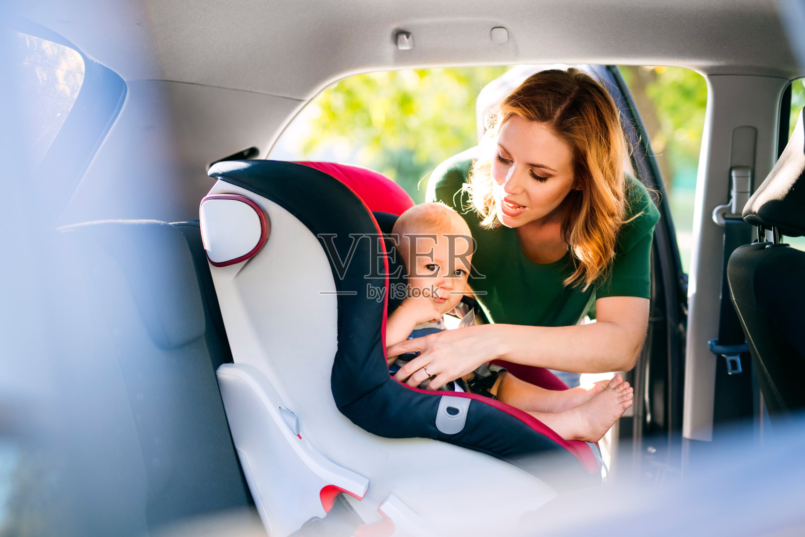 年轻的母亲把小男孩放在汽车座椅上。照片摄影图片