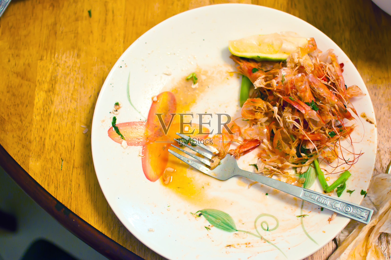 晚餐剩菜。木桌上的白盘子里堆满了红虾的甲壳，上面沾满了酱汁和食物残渣。观念垃圾、废物、有机回收、低效利用食物。俯视图照片摄影图片