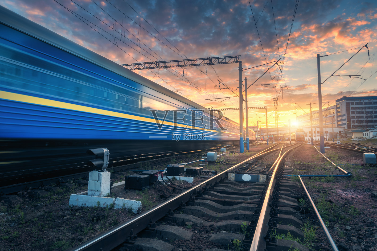 夕阳西下时，铁路轨道上行驶的高速客运列车。火车站里模糊的现代通勤列车，映衬着黄昏时五颜六色的蓝天和红橙相间的云朵。工业景观照片摄影图片